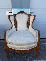Full front view of carved wood wingback chair with cream upholstery
