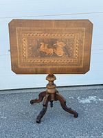 Full view of table with top tilted upright showing marquetry scene and pedestal base