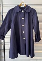 Front view of navy swing coat on hanger showing buttons, collar and overall appearance