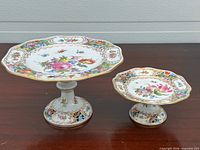 Top view of both pedestal cake plates showing floral decoration and size difference