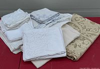Overall view of stacked linens: white cut-work cloth, napkins, beige damask cloth