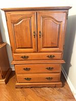 Front view of light brown armoire showing doors, drawers, and hardware