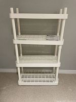 Front view of assembled white plastic 4-shelf unit with manual on shelf