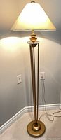 Full view of brass-finish floor lamp with shade illuminated