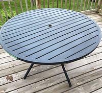 Full view of round slatted metal patio table on deck