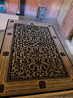 Full view of black and beige floral/vine area rug with Greek-key border