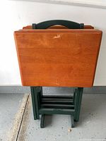 Four wood folding TV trays stacked in matching green storage rack