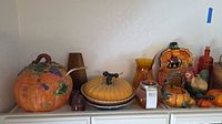 Full shelf view showing majority of items including both large ceramic pumpkins, glass pieces, jar candle and metal ant