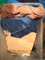 Stack of assorted shirts and jacket in plastic bin showing colours and fabrics