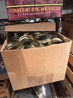 Box containing numerous Ball jar screw bands and lids atop stacked pint jars