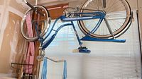 Full view of upside-down blue cruiser bicycle with tassels and chain guard
