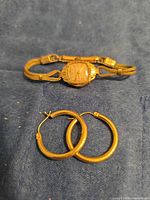 Bulova wristwatch and pair of hoop earrings laid on dark cloth background