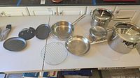All cookware pieces, lids, rack, grill press, grill tray, silicone mitts laid out on table