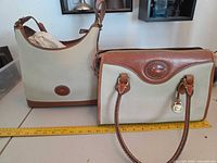 Front view of both Dooney & Bourke handbags showing overall style, color, leather trim and size reference with ruler