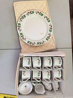 Stack of dinner plates on quilted case with open storage case showing cups, creamer and sugar bowl