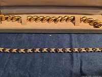 Two gold-tone bracelets, curb link in case and tennis style with black stones below