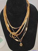 Layered necklaces with pendant, hoops and faux pearls displayed on bust