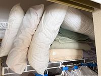 Four white pillows stacked beside three folded blankets on closet shelf