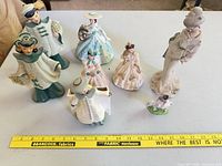 Group of eight assorted porcelain and ceramic figurines displayed with measuring tape showing scale