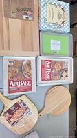 Group view of both AirBake sheets, boxed Rosann ceramic pan, boxed Cuisinart pan, two wooden pizza peels