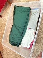 Bin with green track pants over folded grey, white, pink and blue garments
