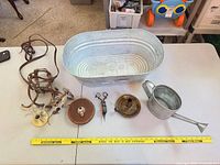 All items laid out: tub, watering can, leather straps, two brass canopies, tape measure, snips, candle holder with measuring stick for scale