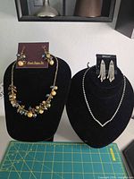 Both necklace/earring sets displayed on busts