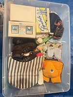 Overview of storage bin showing blanket, boxed shoes, additional shoes, booties, striped hat/bib, plush toy, pacifier, rattle