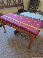 Bench full view showing upholstered top and wood legs with measuring tape indicating length