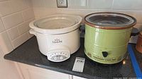 White Rival Crock-Pot and green All American Crockery Cook Pot side by side with lids