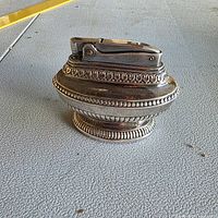 Front view of silver-plated ornate table lighter on textured surface