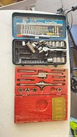 Open blue socket set case showing sockets, ratchet, extensions; red wooden tap and die case below