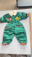 Full view of green toddler snowsuit showing embroidery, pockets, cuffs, collar, zipper, and overall condition
