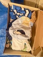 Box containing assorted baby clothes showing striped romper, bib, plush and various garments
