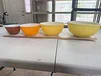 Four nested Pyrex bowls in brown, orange and two yellows aligned by ruler