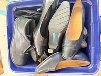 Top view of blue bin containing multiple pairs of black shoes