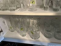 Group of assorted clear highball and tumbler glasses on shelf, showing three size types