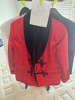 Front view of red velvet tuxedo jacket with black shawl collar, white and black jackets visible behind