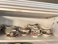 Stacked saucers, sugar bowl with lid, creamer, gravy boat on shelf