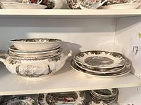 Stack of cereal bowls, oval serving bowl atop, covered two-handled tureen below; additional rimmed soup bowls on same shelf