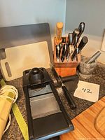 Group shot of knife block with knives, mandoline slicer, cutting boards, sharpener, marble mortar and pestle