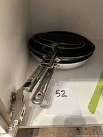 Three nested Lagostina frying pans in cabinet, showing handles and stainless exteriors