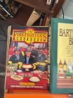 Cover of The Firefighter's Cookbook alongside edge of Bartender's Bible