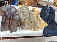 Four jackets laid on sofa: brown faux leather, olive field, tan quilted, navy duffle