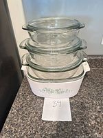 Stacked view of three clear round casseroles with lids atop one white floral casserole