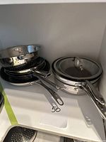 Stacked cookware showing colander, frying pans, saucepans and lids.
