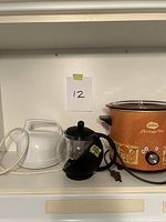 Group shot of slow cooker, kettle, and glass infuser pot on shelf