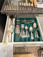 Drawer and countertop view showing mixed flatware and serving pieces
