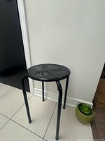 Full view of black metal backless stool with perforated seat and four legs