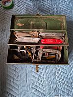 Open green toolbox showing knives and clamps